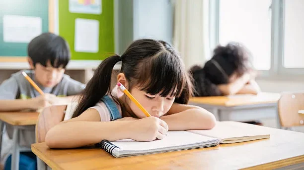 图为小学生在课桌前写字的情景。女学生在小学学习做考试。孩子们在教室里写笔记。教育知识(模糊)图片下载